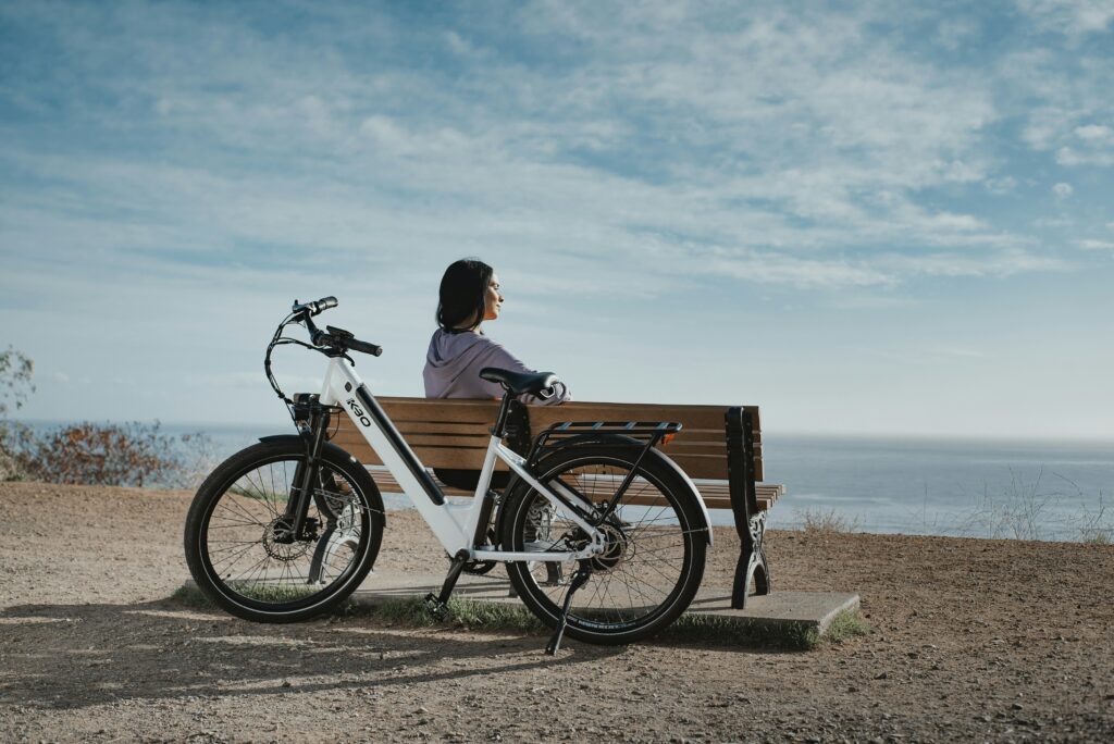 man in black shirt sitting on brown wooden bench beside black and white bicycle during daytime man in black shirt sitting on brown wooden bench beside black and white bicycle during daytime