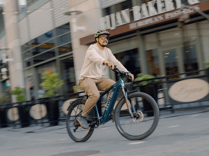 Helmeted rider on an Ocean Blue Velotric Summit 2 beside a bakery Helmeted rider on an Ocean Blue Velotric Summit 2 beside a bakery